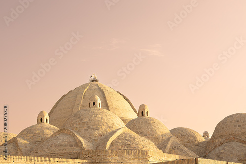 Domed rooftops of Toqi Zargaron bazaar in Bukhara with a stork nest on the central dome. Historic brick architecture bathed in warm sunset light, ideal for travel and heritage publications.