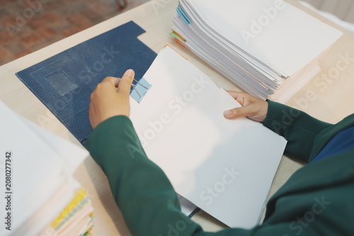 Photos An office employee standing behind a light wooden desk uses both hands to lift and vertically align a heavy stack of white document