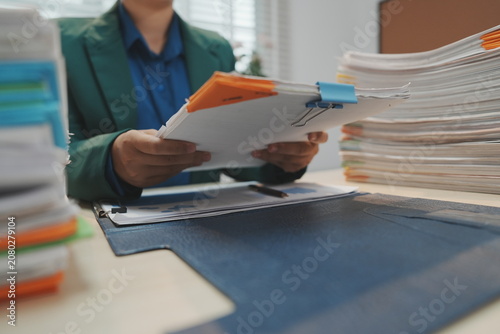 Fotografi An office employee standing behind a light wooden desk uses both hands to lift and vertically align a heavy stack of white document