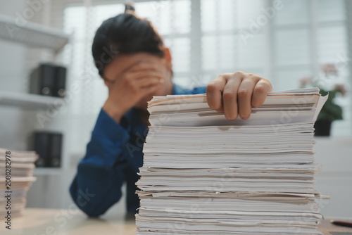 Принти на полотні An office employee standing behind a light wooden desk uses both hands to lift and vertically align a heavy stack of white document