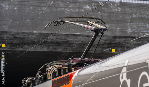 Close up of electric train pantograph connecting to overhead power lines in railway station.