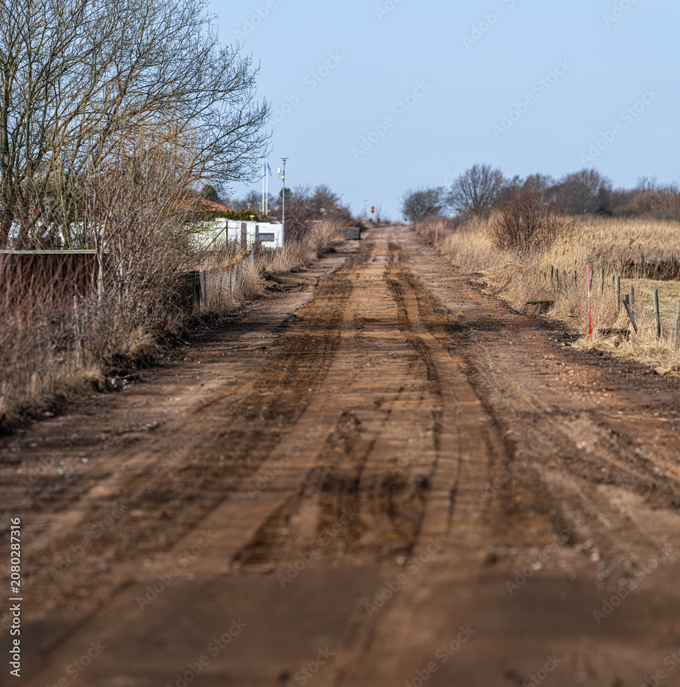 Fototapeta premium Muddy rural dirt road stretching through dry grass landscape with distant horizon Nature.