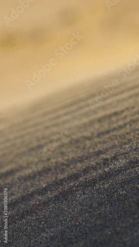 Fine dark sand texture with shallow depth of field, close up view of wind shaped beach surface creating abstract natural pattern 