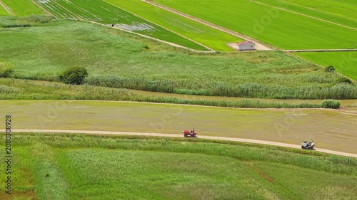 Young rice fields and wetland landscape in Ebro Delta Natural Park, Spain. Aerial drone view of agricultural land, irrigation channels and farm vehicles working along rural roads 