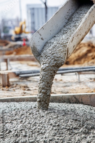 Wet cement pouring from a mixer chute at a construction site, close up of liquid concrete flowing down into a foundation formwork, heavy building industry concept