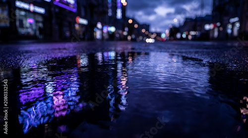 City neon light reflections in wet street puddle.
