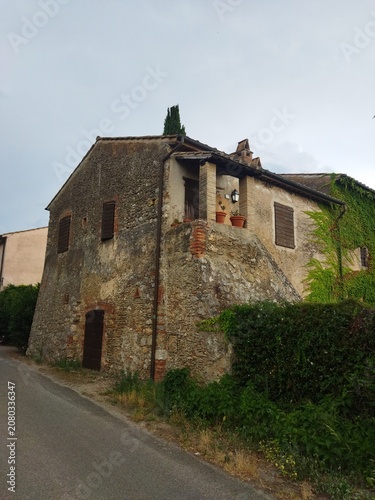 Antigua casa rústica de piedra y ladrillo con contraventanas de madera y fachada cubierta de hiedra, Toscana, Italia.