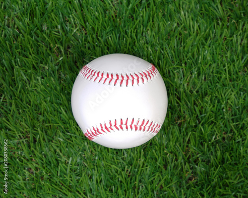A white baseball with red stitching on the grass