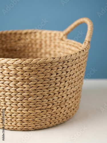 Woven wicker storage basket with handle on blue background, interior organization, home decor, decluttering, rustic style
