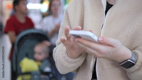 Person holds phone, fingers scrolling, focused. Background shows blurred people and lights. Scene captures modern urban life, digital interaction. Ideal for tech, communication, or lifestyle themes