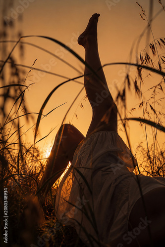 Barfüßige Frau entspannt in einer Blumenwiese bei Sonnenuntergang. Stimmungsvolles Lifestyle-Motiv zu Sommer, Freiheit, Natur, Achtsamkeit, Wellness, Entspannung und Slow Living.