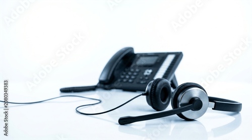 Call center workspace showing black operator headset with blurred office telephone in background.