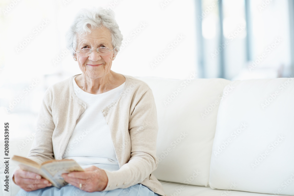 Obraz premium Relax, portrait or old woman in home with book, fantasy reading or insight in literature hobby. Space, glasses or senior person on sofa with fairytale, peaceful moment or fiction story in retirement.
