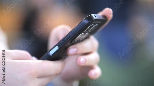 Hands grip phone, thumbs scroll. Focus on interaction, not face. Blurred background suggests public space. Ideal for mobile app, social media, or digital communication themes