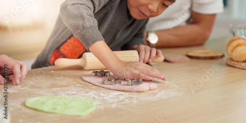 Quadro su tela Asian boy using cookie cutters on dough for family baking activity