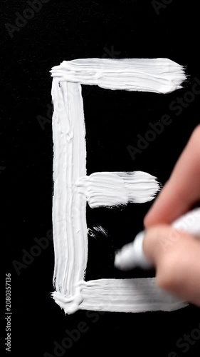 Hand writing white letter E on black background.