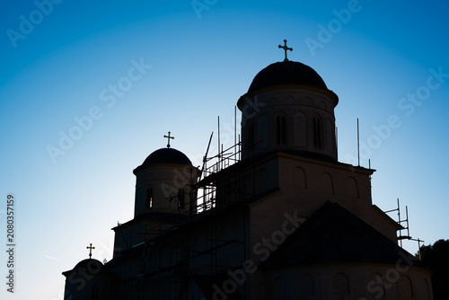 Silhouette of an orthodox church building with domes and crosses against a blue twilight sky. Low angle view of a Christian monastery during sunset or sunrise.
