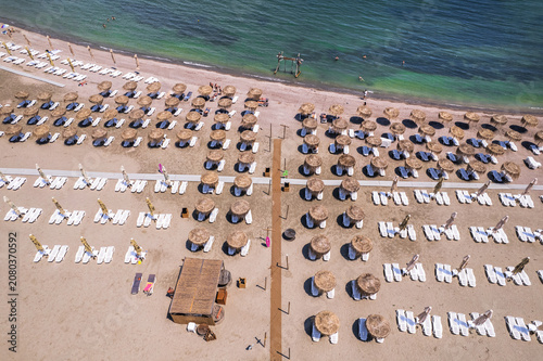 Aerial top down view of an organized sandy beach resort with rows of straw umbrellas and white sun loungers near the sea. Aerial top down view of rows of straw umbrellas and sun loungers on a sandy be