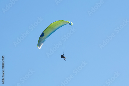 Vol en parapente dans un ciel bleu azur d'été en montagne. Voile jaune et bleue.