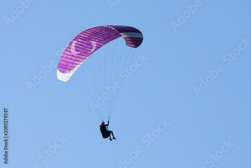 Vol en parapente dans un ciel bleu azur estival en montagne. Voile violette et blanche.