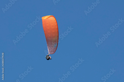 Vol en parapente dans un ciel bleu azur d'été en montagne. Voile orange.