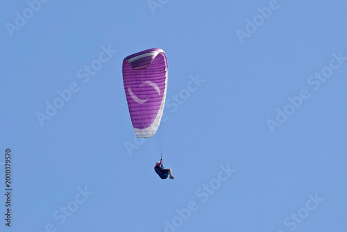 Vol en parapente dans un ciel bleu azur d'été en montagne. Voile violette et blanche.
