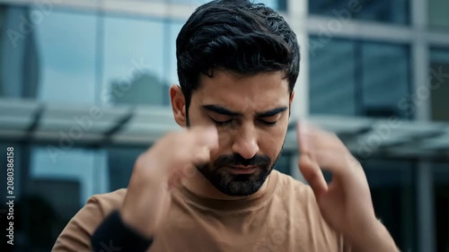 Young man experiencing stress or anxiety, rubbing his temples in a moment of distress outdoors.