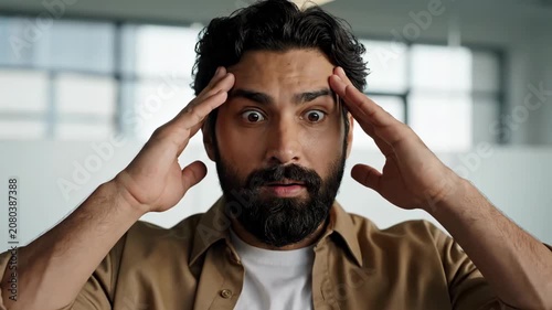 Stressed young man with a beard holding his head in his hands, looking overwhelmed and frustrated.