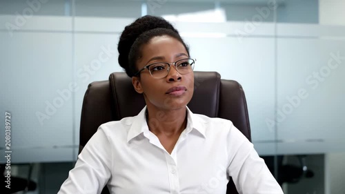 Serious African American businesswoman in glasses sitting in office.