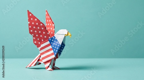 Patriotic origami bald eagle folded from American flag patterned paper standing on a blue studio surface celebrating 4th of July Independence Day holiday theme