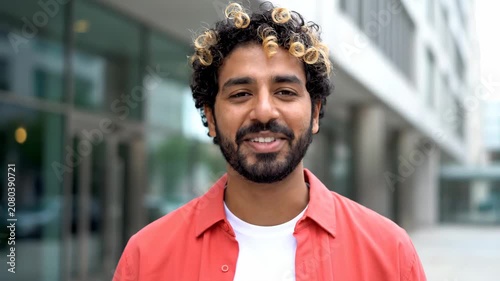 Smiling young man with curly hair looking directly at the camera outdoors.
