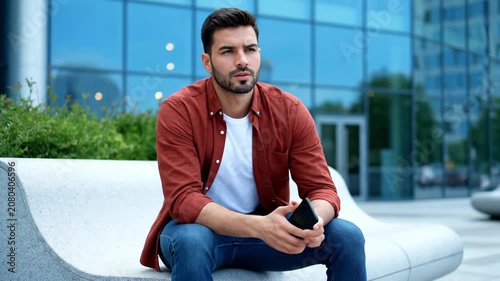Thoughtful young man sitting on a modern bench outdoors, looking away with a pensive expression.