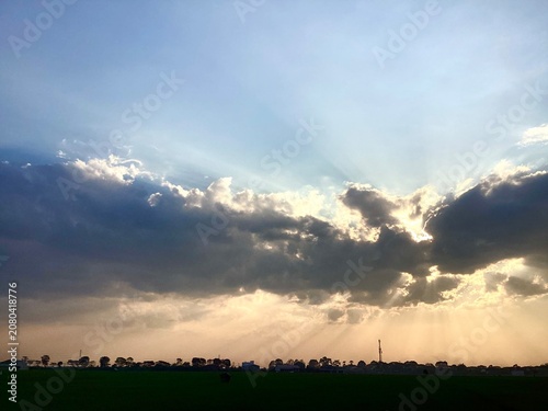 sunlight shining through the gaps in the black clouds, a beautiful sunset in the rice field area
