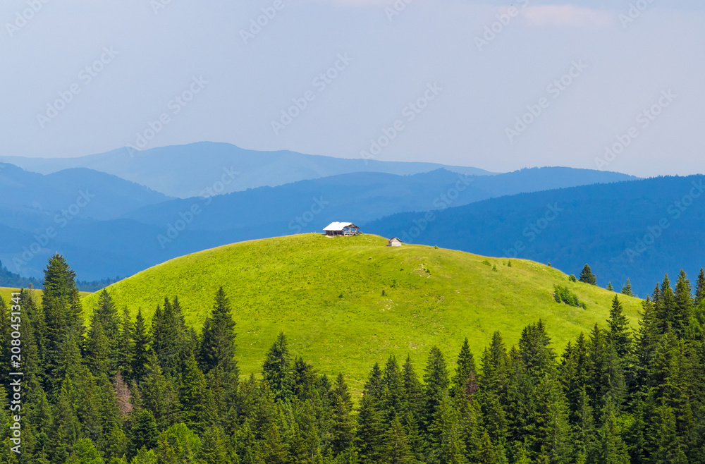 Obraz premium Breathtaking scene captures a tranquil wooden cabin nestled atop a vibrant green hill in the Carpathian Mountains. Landscape with a cabin on top of a mountain hill