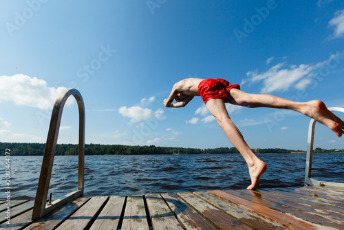 Slika na platnu Person performs an acrobatic dive off a dock into a lake on a sunny summer day