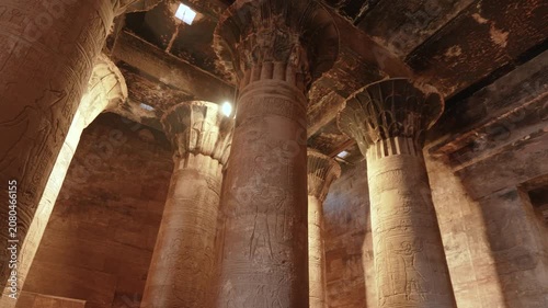 Interior view of the hypostyle hall at the Temple of Edfu in Egypt, featuring massive stone columns decorated with intricate ancient Egyptian hieroglyphs.
