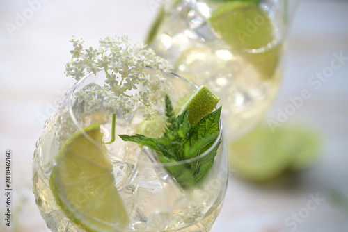Wine cocktail spritz called Hugo made from prosecco, syrup and soda, garnished with elderflowers, mint leaves and lemon slices in a drinking glass, selected focus