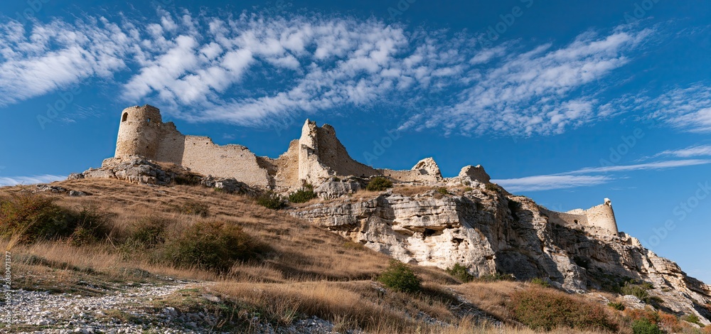 Fototapeta premium Ruins of an ancient stone fortress perched on a hill beneath a clear sunny sky, symbolizing history and exploration.