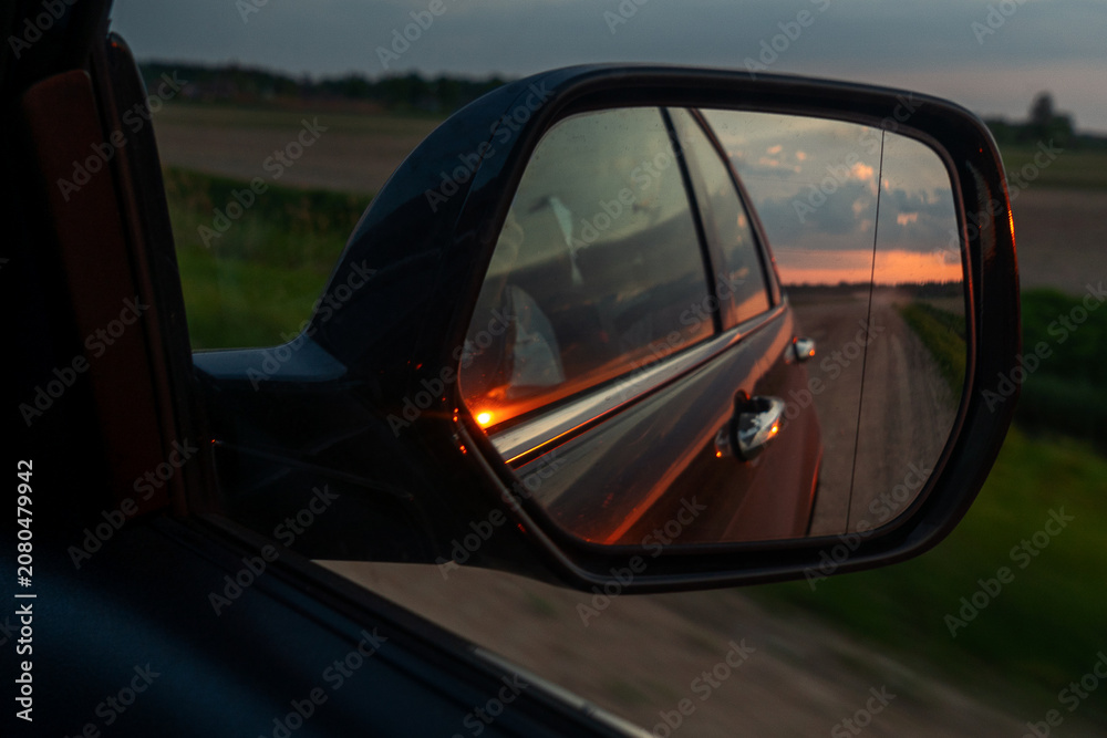 Fototapeta premium Freedom and travel concept with scenic orange sunset clouds reflected in automobile wing mirror on a rural evening way