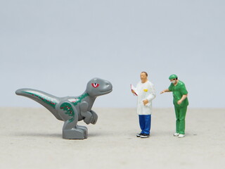Mini toy of action figure at table with blur background. Miniature photography concept design. Minifigure of scientist doctor character with baby dino at nature.