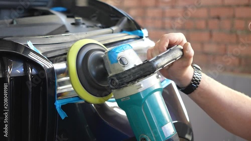 Man polishes the glass of a car headlight with a polishing machine from small scratches, chips. Process polishing of the front car headlights. Hands of male professional worker with orbital polisher. 