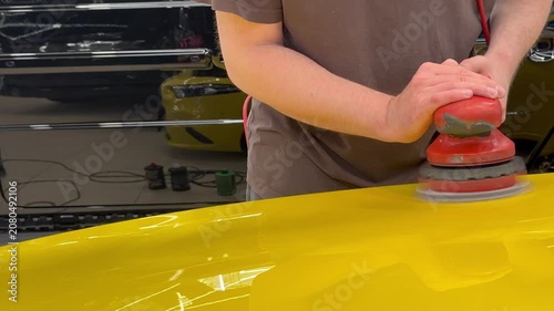 A car service worker polishes the car body with a polishing machine. Detailing and polishing of the car. Car detailing - hands with an orbital polishing machine in an auto repair shop. 