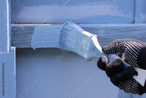 human hand wearing black gloves holding a brush painting fence with light-blue paint