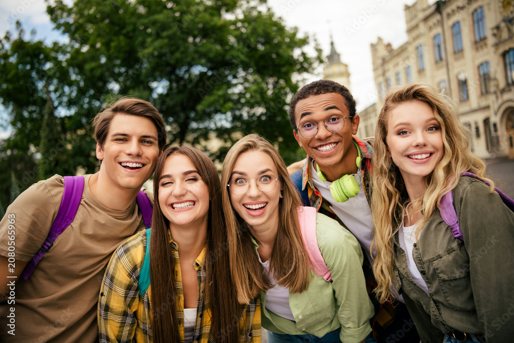 Obraz premium Five smiling college friends posing together on campus with backpacks, diversity, and cheerful energy as they prepare for classes and hang out in an outdoor university setting
