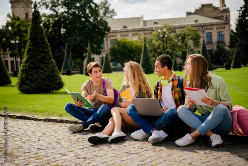 Four college students studying together outdoors on campus, sharing notes, a laptop and conversation
