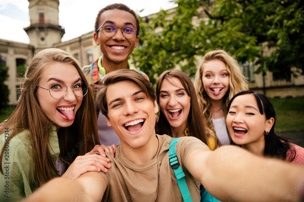 Fototapeta premium Group of happy students taking a playful selfie on a college campus, laughing friends enjoying time together outdoors