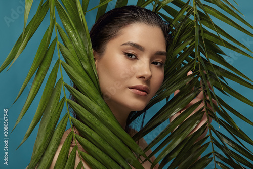 Photos Well groomed woman peeks out from behind palm leaves.