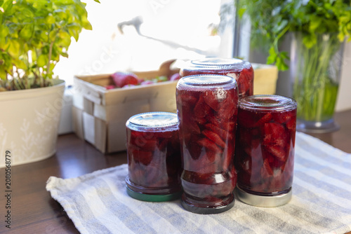 Glass jars of homemade strawberry jam on the kitchen table, homemade preserves of fresh berries in summer