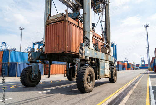 Container terminal straddle carrier lifting cargo in shipping yard  