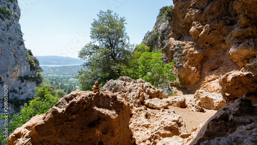 Scenic view from a rocky mountain cave overlooking a green valley and lake.